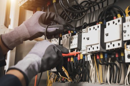 Electricity and electrical maintenance service, Engineer hand holding AC multimeter checking electric current voltage at circuit breaker terminal and cable wiring main power distribution board.